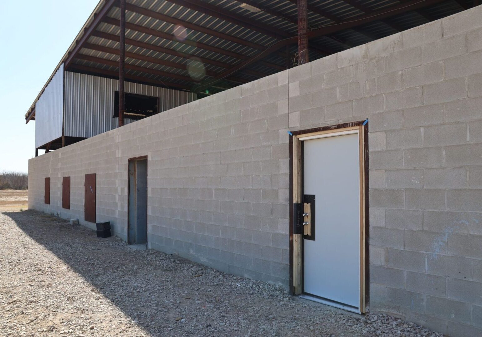 Exterior shoot house wall with a standard training door fitted with the Breach Pro Modular Breaching Insert (MBI), allowing repeated mechanical breaching drills using a real door frame and resettable lockset system.